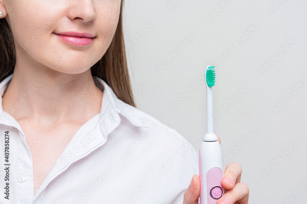 Woman shows an electric toothbrush, white background. Concept of caring for the oral cavity and healthy teeth with an smart toothbrush, cropped image Woman shows an electric toothbrush, white background. Concept of caring for the oral cavity and healthy teeth with an smart toothbrush, cropped image