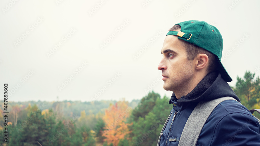 Young guy with a backpack standing in a forest at sunrise, guy looks into the distance, copy space, 16:9 Young guy with a backpack standing in a forest at sunrise, guy looks into the distance, copy space, 16:9