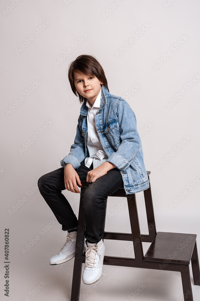 Handsome fashion little boy sits on a chair in studio. Model Test. Fashion and people concept