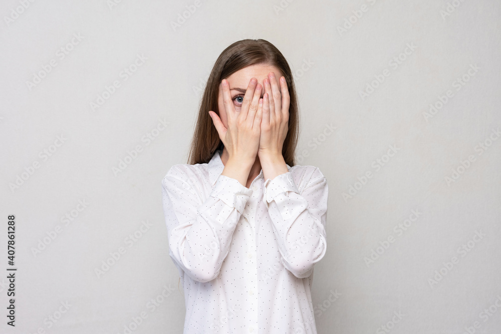 Portrait of a afraid woman peeking through her fingers, white background, copy space Portrait of a afraid woman peeking through her fingers, white background, copy space