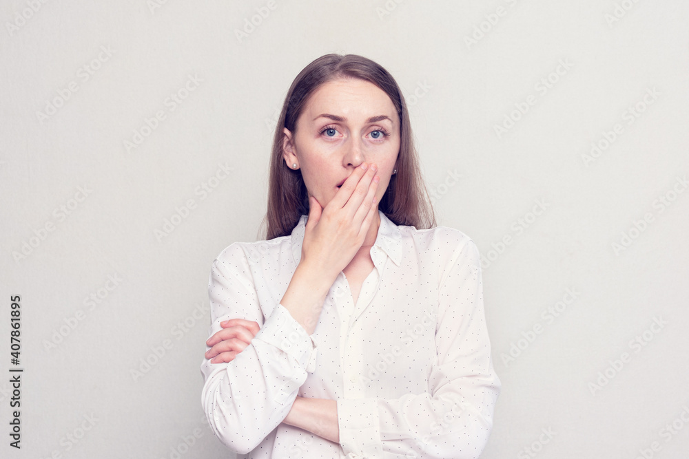 Scared girl covers her mouth with her hand in horror, looks at the camera, white background Scared girl covers her mouth with her hand in horror, looks at the camera, white background