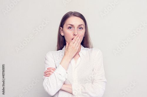 Scared girl covers her mouth with her hand in horror, looks at the camera, white background