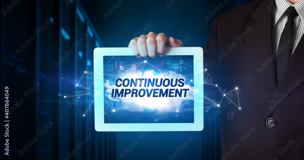 Young business person working on tablet and shows the inscription: CONTINUOUS IMPROVEMENT Young business person working on tablet and shows the inscription: CONTINUOUS IMPROVEMENT
