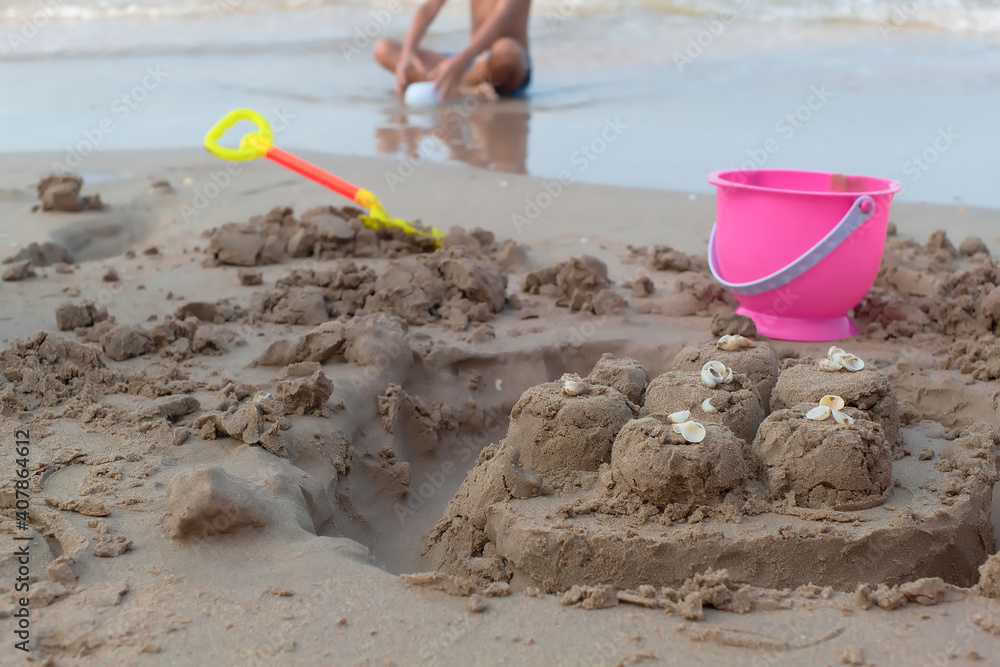 Boy put sand toys like pink plastic buckets, yellow and orange shovel. Used to build a sand castle decorated with white seashells at a clear beach. Boy put sand toys like pink plastic buckets, yellow and orange shovel. Used to build a sand castle decorated with white seashells at a clear beach.