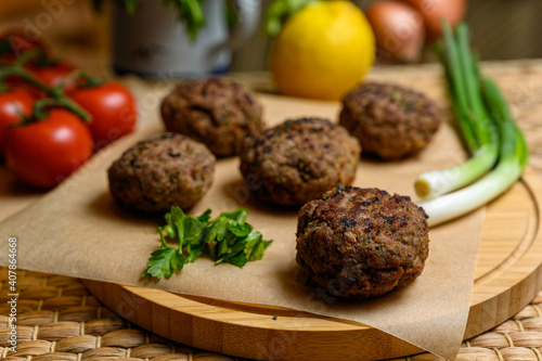 Homemade fried meatballs, served on wooden cutting board with tomatoes, onions and parsley