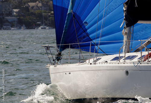 A 38-foot sailboat in Sydney Harbor with its bright blue spinnaker fully deployed on a port tack. View of the boat's bow