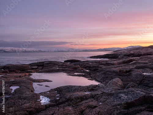 Wonderful mountain landscape with a Cape on the shore of the Barents sea. Amazing sunrise landscape with polar white snowy range of mountains.