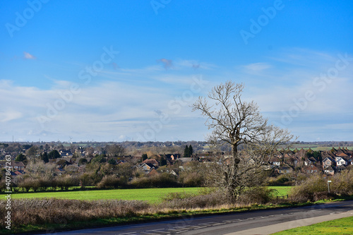 Landscape with a green field and blue sky, with a small town in the background.