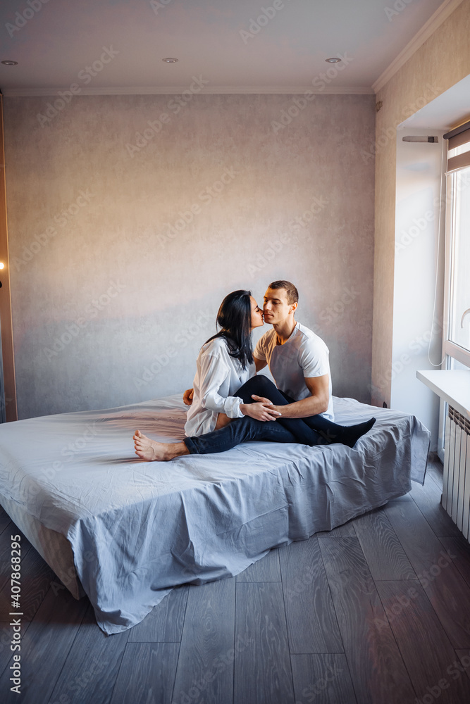 Attractive, young couple of lovers having sex at home in the bed in bright room. Girl kissing her boyfriend oddly, gently pulling back his lower lip. Celebrating Valentine's Day - February 14 Attractive, young couple of lovers having sex at home in the bed in bright room. Girl kissing her boyfriend oddly, gently pulling back his lower lip. Celebrating Valentine's Day - February 14