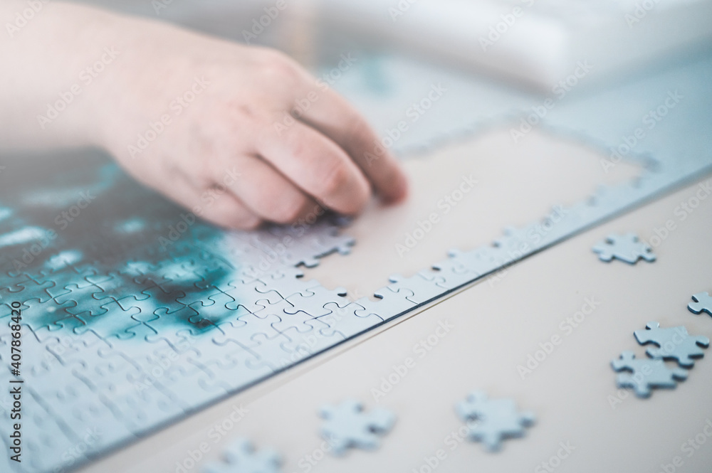 Hands of woman with puzzle on the table. Hand holding piece of puzzle on white background. Hands of woman with puzzle on the table. Hand holding piece of puzzle on white background.