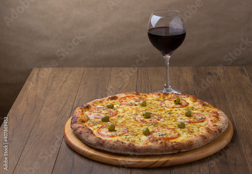 Delicious mozzarella cheese pizza with red tomato slices. A glass of red wine to accompany. Made in the wood oven. Horizontal photograph with space for texts on the left.