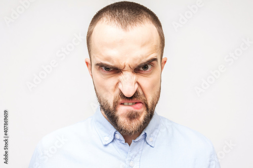 Bearded angry, portrait of an evil young man with a grimace on his face, white background, close-up