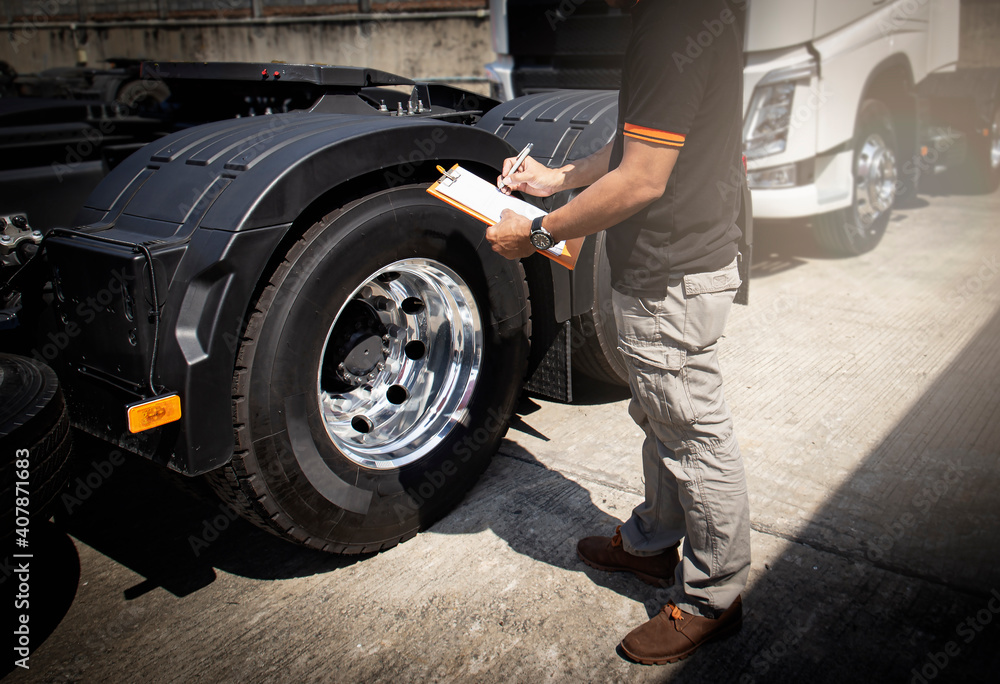 Truck driver holding clipboard his inspecting daily checklist safety of a truck wheels and tires. Semi truck freight transportation.