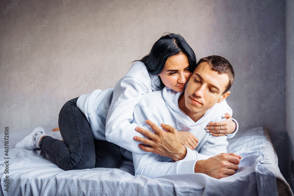 Cute, charming, attractive young Europeans man and woman lie relaxed on the bed. Looking out the window, hug, stroke each other. Foreheads, faces together, kiss. Tenderness at home Cute, charming, attractive young Europeans man and woman lie relaxed on the bed. Looking out the window, hug, stroke each other. Foreheads, faces together, kiss. Tenderness at home