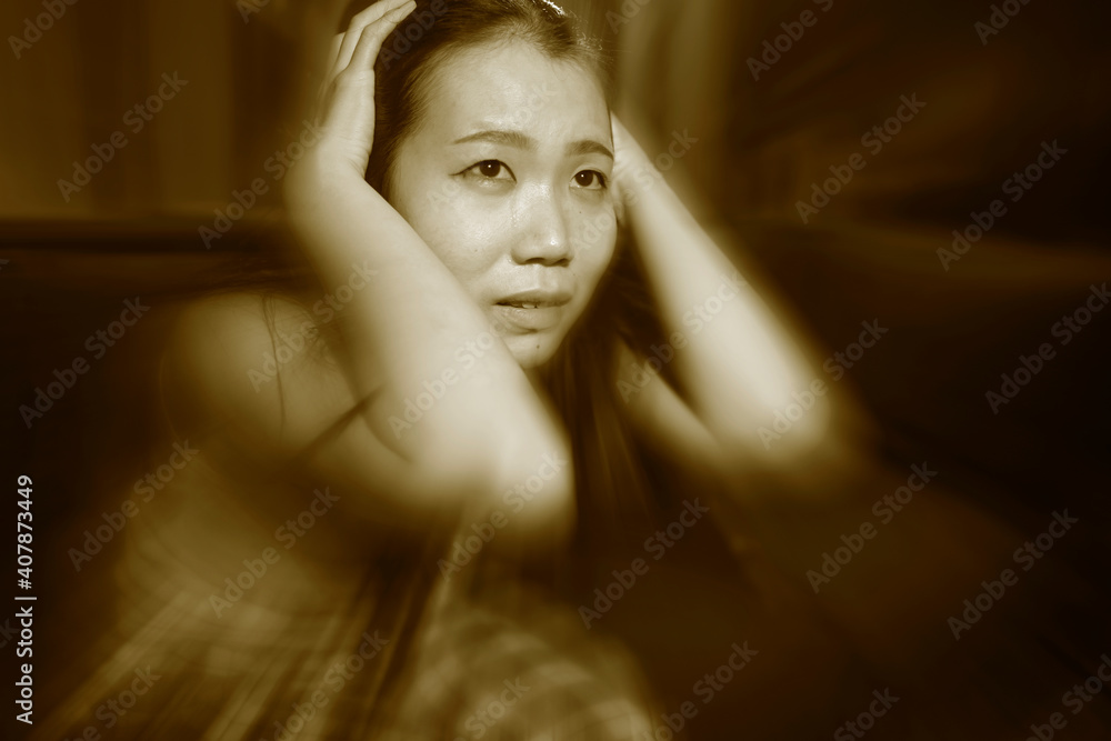 Asian woman suffering depression - dramatic artistic portrait of young beautiful sad and depressed Chinese girl in pain helpless on couch at home in the dark