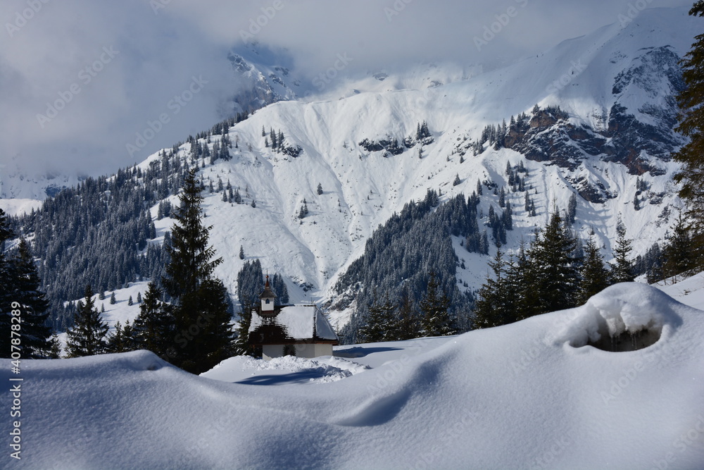 Small chapel at the foot of mountains covered with plenty of snow in winter