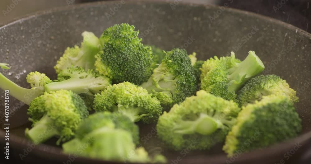 Pouring broccoli inflorescence into hot frying pan. Close up Pouring broccoli inflorescence into hot frying pan. Close up
