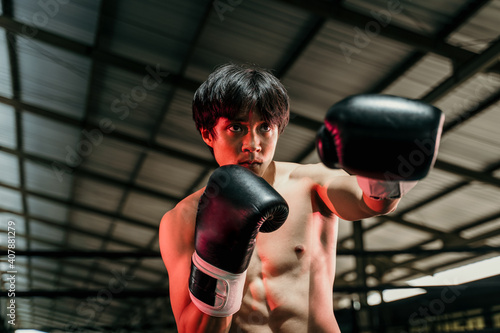 Strong young man stand wearing boxing gloves with punch in the boxing ring