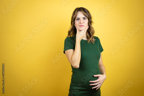Young beautiful brunette woman pregnant expecting baby over isolated yellow background touching painful neck, sore throat for flu, clod and infection