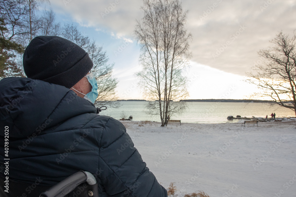 A man in a wheelchair in a medical mask, walking by the sea. A man in a wheelchair in a medical mask, walking by the sea.