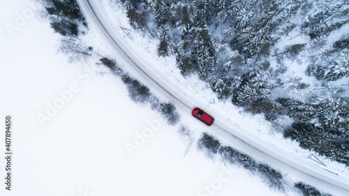 Aerial top view of snow covered forest and lake with winter road and red car. Drone photography landscape. © raland
