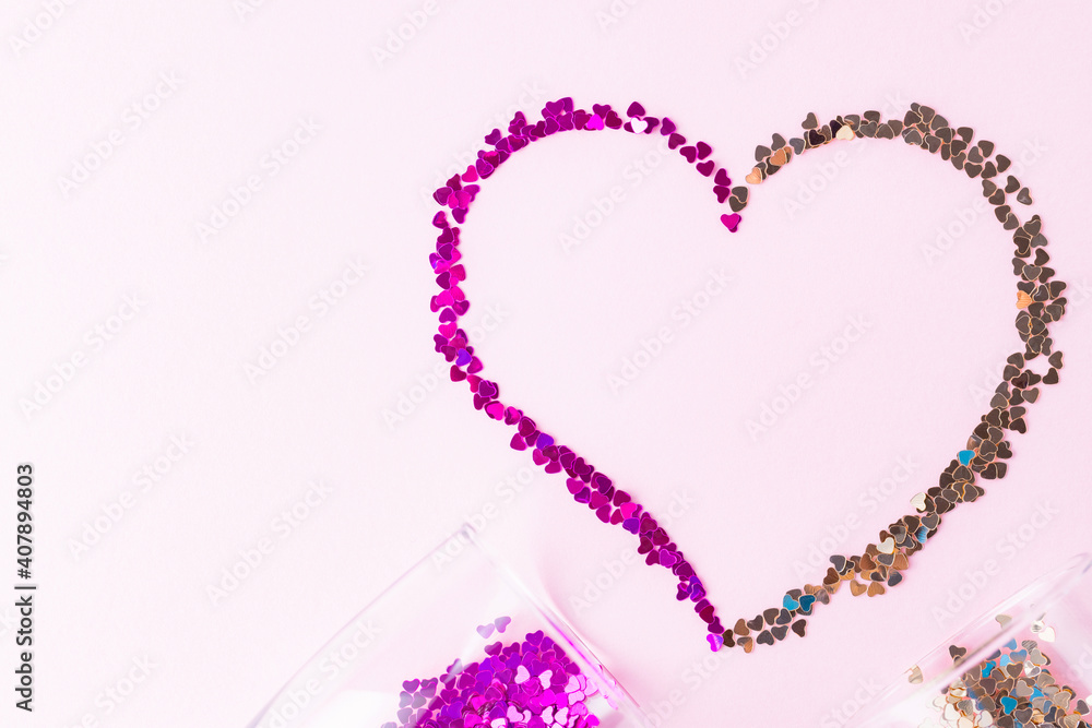 Heart shape made of multicolored glitter. Two champagne glasses with splash of heart shaped confetti over pink background. Valentine's Day concept. Flat lay