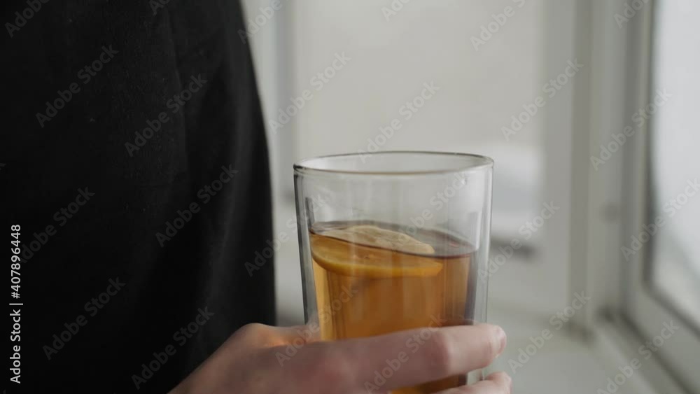 Close-up caucasian man holding and twirling large glass transparent double bottom cup with lemon tea on balcony Close-up caucasian man holding and twirling large glass transparent double bottom cup with lemon tea on balcony