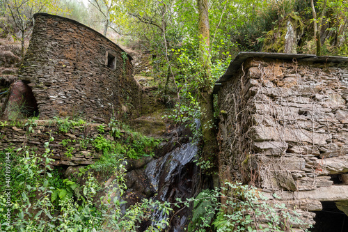 Watermill in the middle of a forest. Rustic building made of rock. Small waterfal.