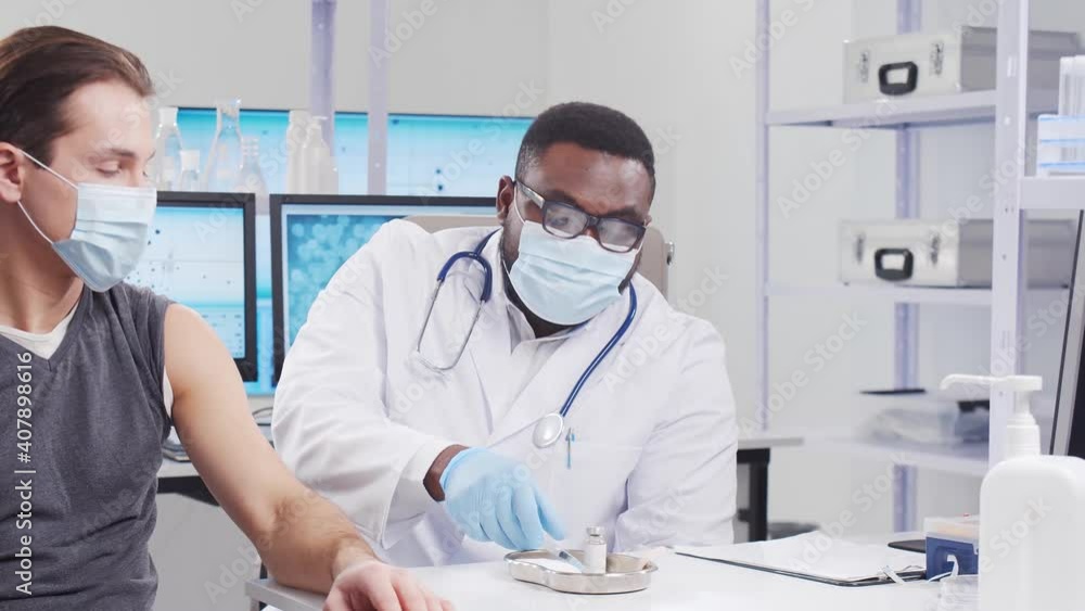 African-American doctor makes a coronavirus vaccine using a syringe and hypodermic needle. Medical worker and patient at the hospital office. Vaccination and safety concept. African-American doctor makes a coronavirus vaccine using a syringe and hypodermic needle. Medical worker and patient at the hospital office. Vaccination and safety concept.