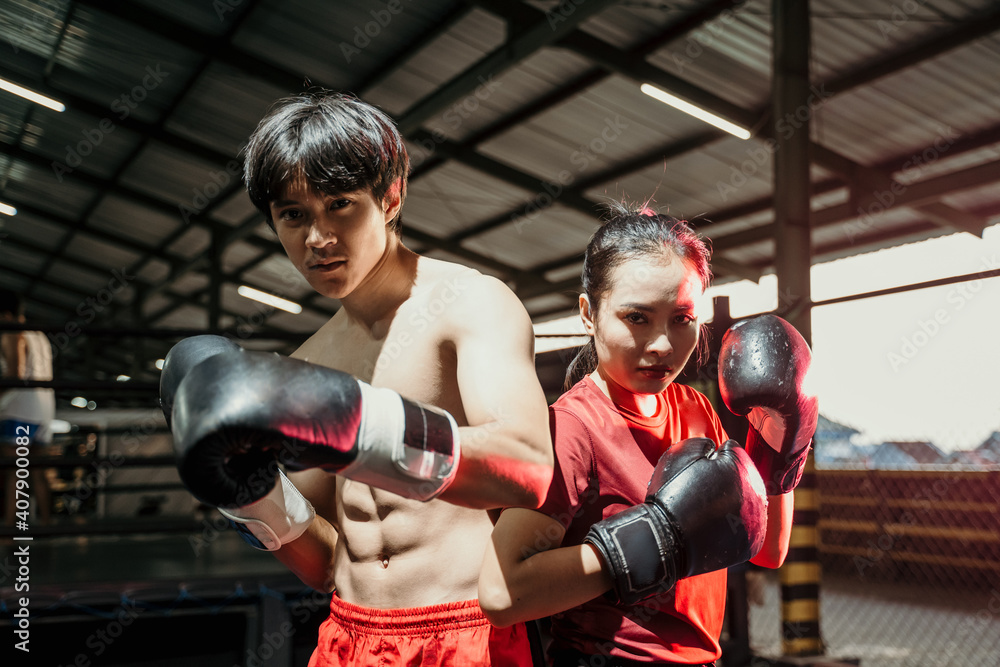 Asian female and male boxers stand in boxing gloves with back to back in the boxing ring
