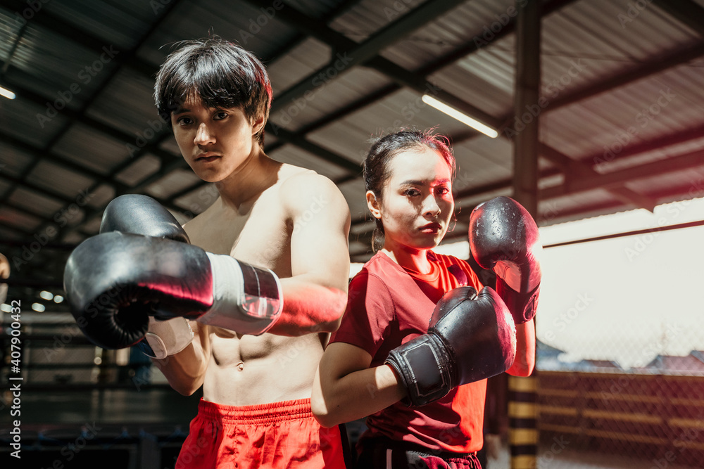 Female and male fighters stand in boxing gloves and pose back to back in the ring Female and male fighters stand in boxing gloves and pose back to back in the ring