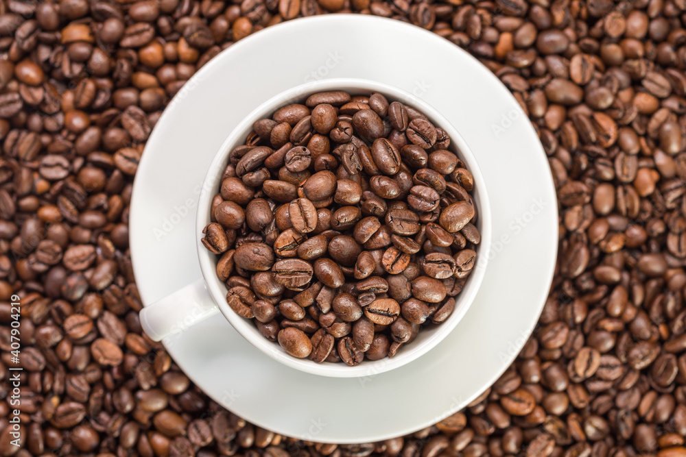 A white coffee cup full of fresh coffee beans on roasted coffee beans background top view A white coffee cup full of fresh coffee beans on roasted coffee beans background top view