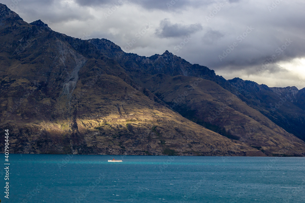 Obraz premium Ship on Lake Wakatipu on a cloudy day next to beautiful sun rays, Queenstown, New Zealand