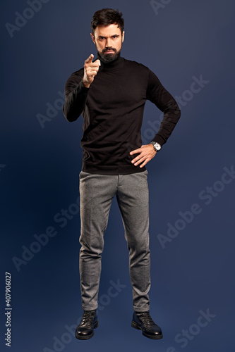 Young bearded stylish teacher or business man pointing finger at camera. Full body length portrait isolated on Pacific Blue studio background.