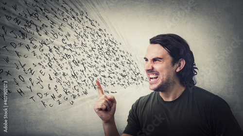 Angry man reacting furious clenching teeth screaming and shaking his index finger. Irritated and annoyed guy negative facial expression, blaming or scolding as multiple text letters come out his mouth photo