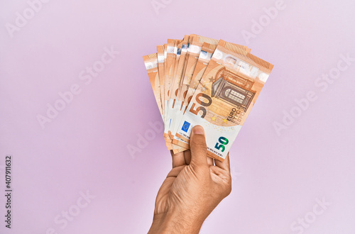 Hispanic hand holding 50 euro banknotes over isolated pink background.