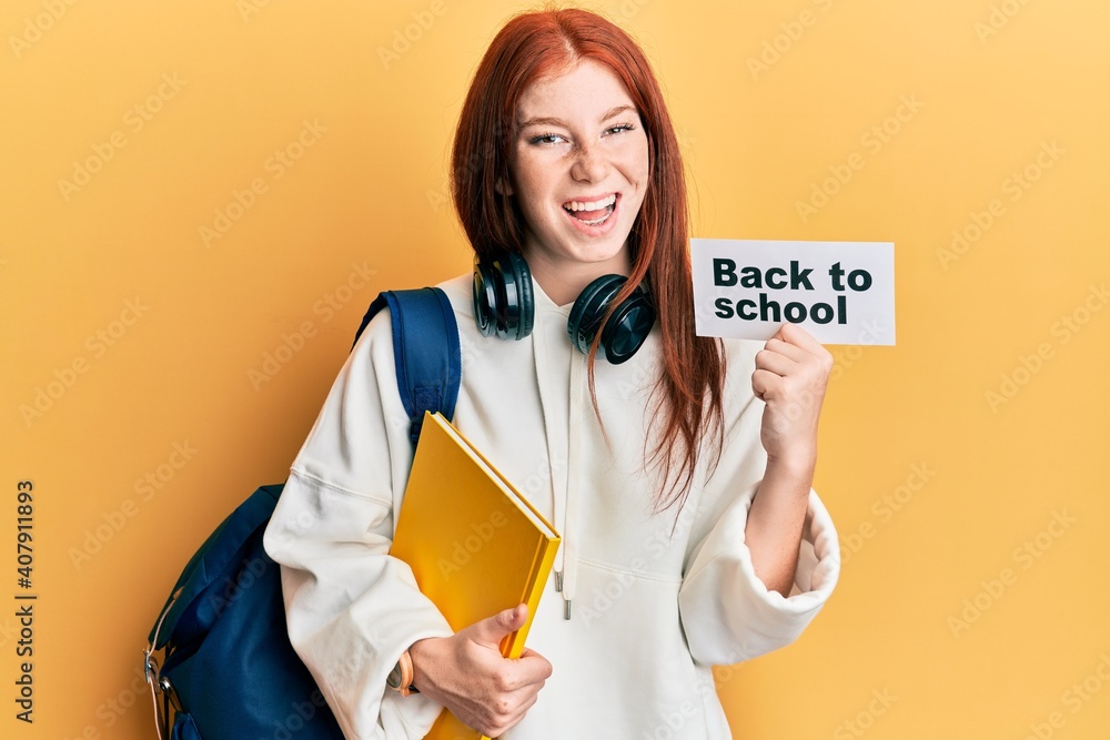 Young red head girl wearing backpack holding back to school banner smiling and laughing hard out loud because funny crazy joke. Young red head girl wearing backpack holding back to school banner smiling and laughing hard out loud because funny crazy joke.