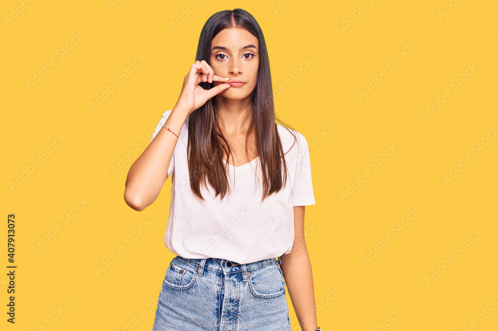 Young hispanic woman wearing casual white tshirt mouth and lips shut as zip with fingers. secret and silent, taboo talking Young hispanic woman wearing casual white tshirt mouth and lips shut as zip with fingers. secret and silent, taboo talking