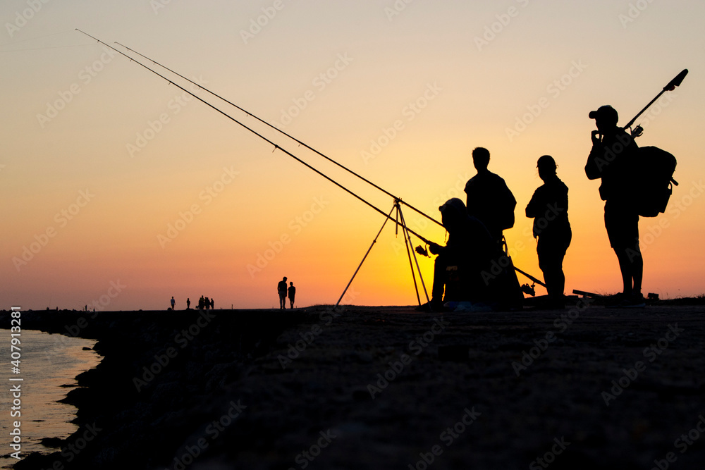 Silhouette of friends are fishing under sunset of a ocean