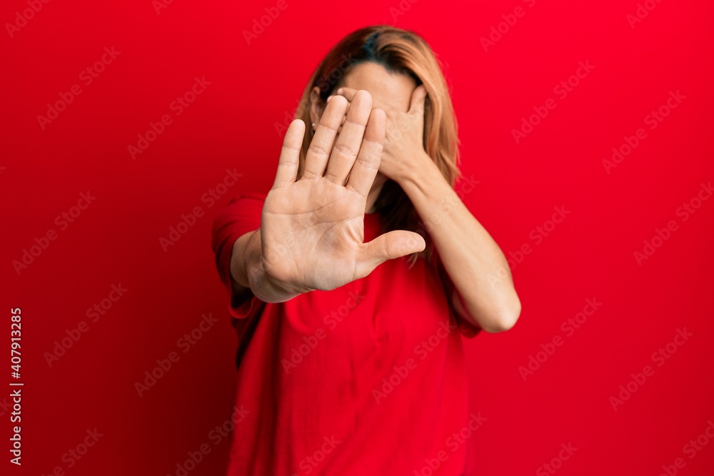 Hispanic young woman wearing casual red t shirt covering eyes with hands and doing stop gesture with sad and fear expression. embarrassed and negative concept. Hispanic young woman wearing casual red t shirt covering eyes with hands and doing stop gesture with sad and fear expression. embarrassed and negative concept.