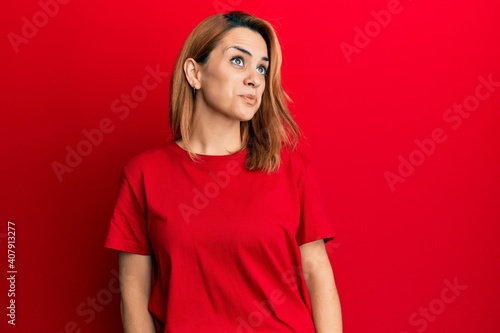 Hispanic young woman wearing casual red t shirt smiling looking to the side and staring away thinking. © Krakenimages.com