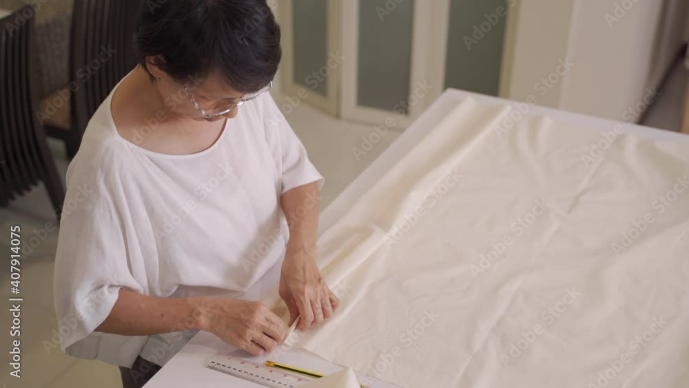 asian senior woman doing garment DIY projects at home. home activity during covid-19 pandemic. measuring, marking, and cutting fabric process. asian senior woman doing garment DIY projects at home. home activity during covid-19 pandemic. measuring, marking, and cutting fabric process.