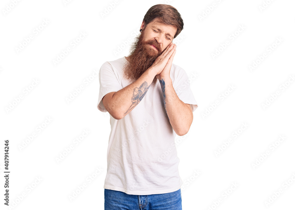 Handsome young red head man with long beard wearing casual white tshirt sleeping tired dreaming and posing with hands together while smiling with closed eyes. Handsome young red head man with long beard wearing casual white tshirt sleeping tired dreaming and posing with hands together while smiling with closed eyes.