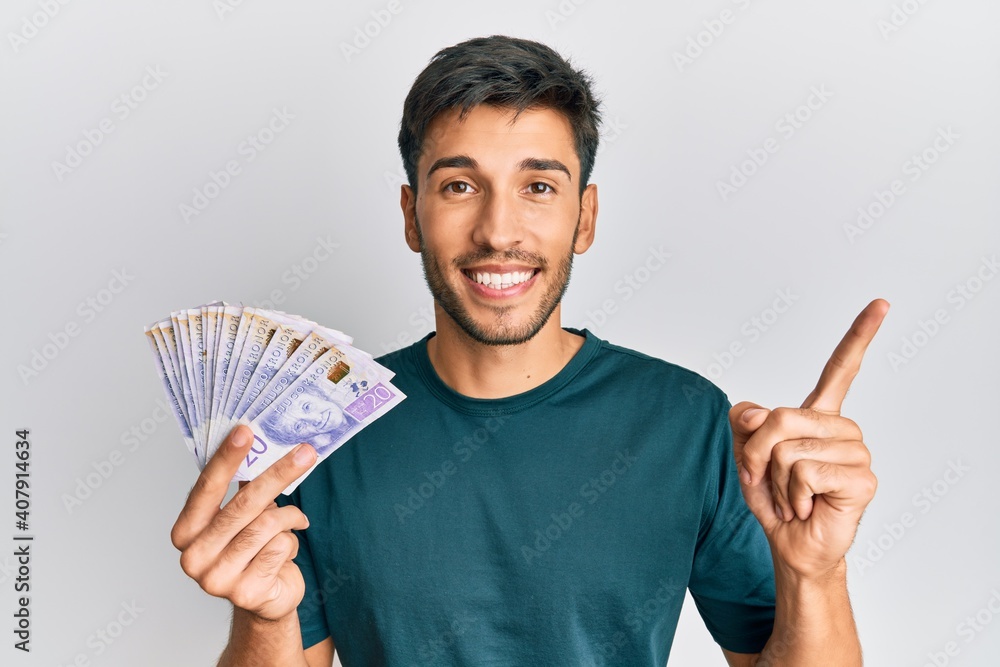 Young handsome man holding 20 swedish krona banknotes smiling happy pointing with hand and finger to the side Young handsome man holding 20 swedish krona banknotes smiling happy pointing with hand and finger to the side