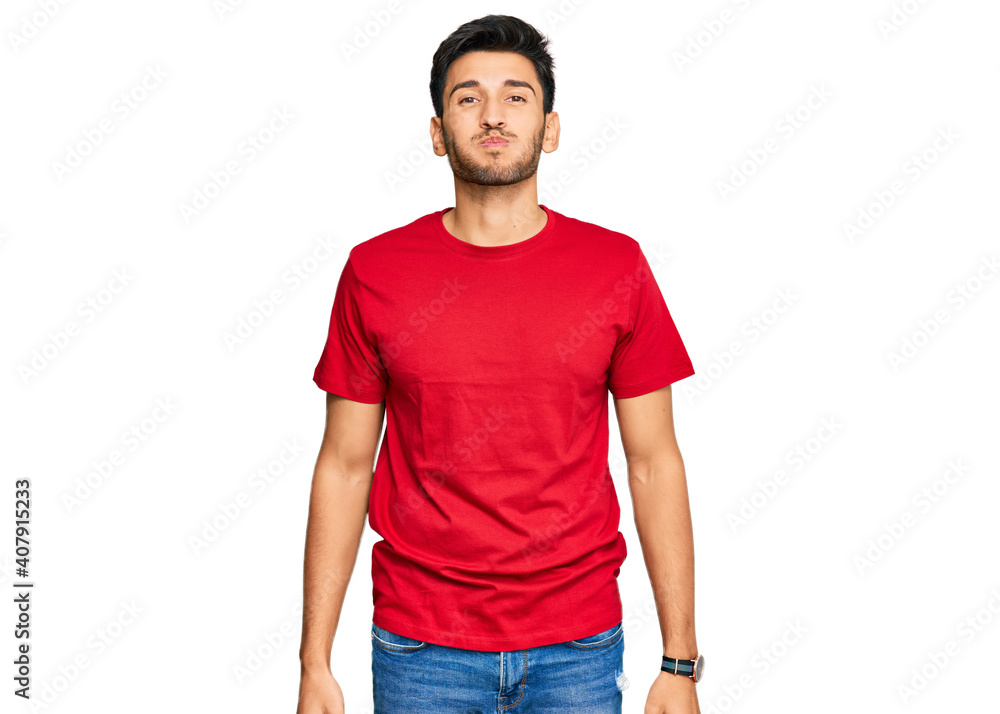 Fototapeta premium Young handsome man wearing casual red tshirt puffing cheeks with funny face. mouth inflated with air, crazy expression.