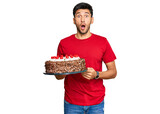 Young handsome man celebrating birthday with cake scared and amazed with open mouth for surprise, disbelief face