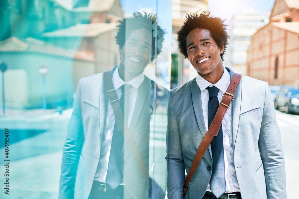 Fototapeta premium Young handsome african american businessman wearing suit smiling happy. Leaning on the wall with smile on face at town street.