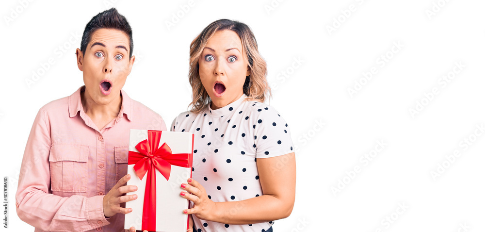 Couple of women holding gift scared and amazed with open mouth for surprise, disbelief face Couple of women holding gift scared and amazed with open mouth for surprise, disbelief face