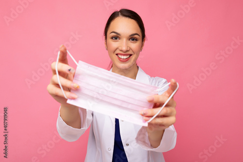 Happy young woman holds and wears a white medical mask to protect yourself from corona virus, cares for her health and safety, sticks to self-isolation. Concept of Covid-19 photo