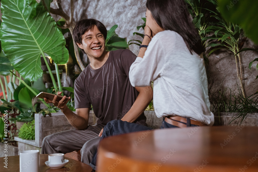 Fototapeta premium Cheerful couple laughing sitting in a coffee shop when holding a smart phone
